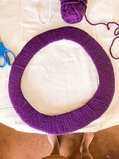 Wreath base with purple yarn wrapped around it