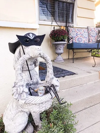 Dog statue with a mask and hat holding a spider in a basket