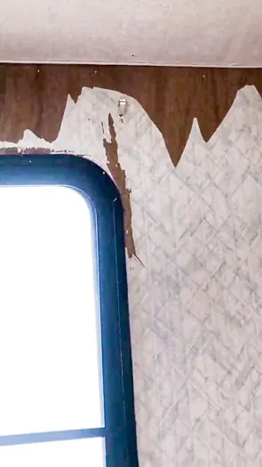 Window on the left side with wallpaper peeling on the wall to show wood.