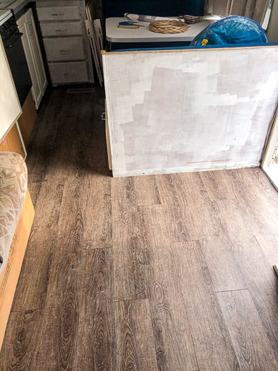 inside of a camper with vinyl flooring and unpainted cabinets