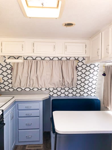Front of a trailer with blue lower cabinets, white upper cabinets, and scalloped wallpaper.