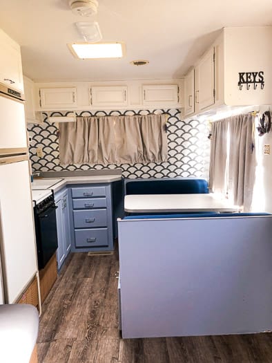 Full view of the front of a trailer with blue lower cabinets, white upper cabinets, and scalloped wallpaper.