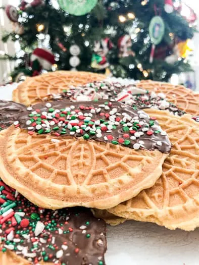 pizzelles with chocolate and sprinkles on top in front of the Christmas tree