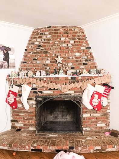Brick fireplace with a little Christmas village on the mantel and stockings hanging