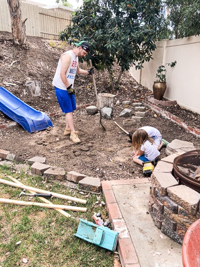 Man cleaning up dirt area while kids play in the foreground.