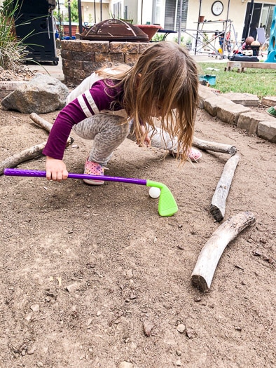 Little girl playing with a golf club on the mini golf course