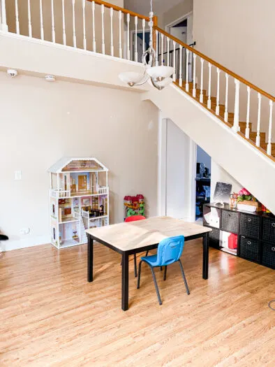 Table in the forefront with stair railings above. Stair railings are orange wood on the top and bottom with white balusters.