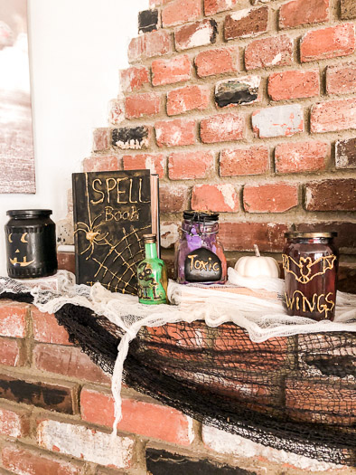 Brick fireplace with pumpkin jar, spell book, and 3 poison bottles sitting on the mantel.
