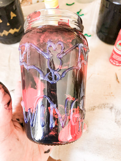 A jar with red and black marbled paint inside. The outside has a bat and the word wings made out of hot glue.