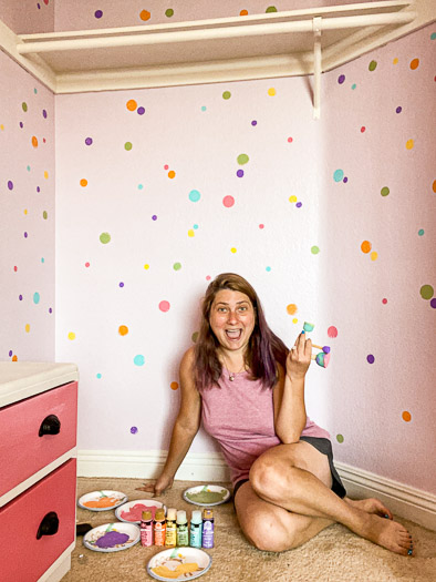 woman holding paint daubers sitting in front of pink multi polka-dotted wall in closet