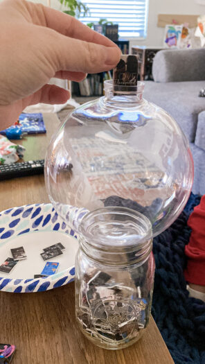 Mini book being dropped into a clear ornament that is sitting on a mason jar filled with mini books.