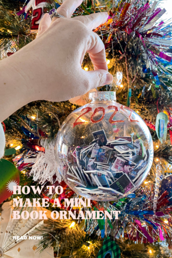 Hand holding a clear ornament with mini books inside and the year 2022 in glitter glue written on the ornament