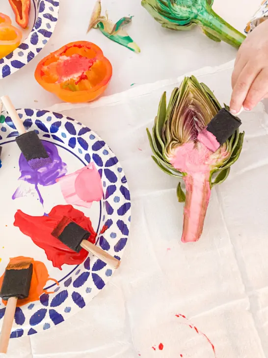 A hand painting a artichoke pink with a sponge brush