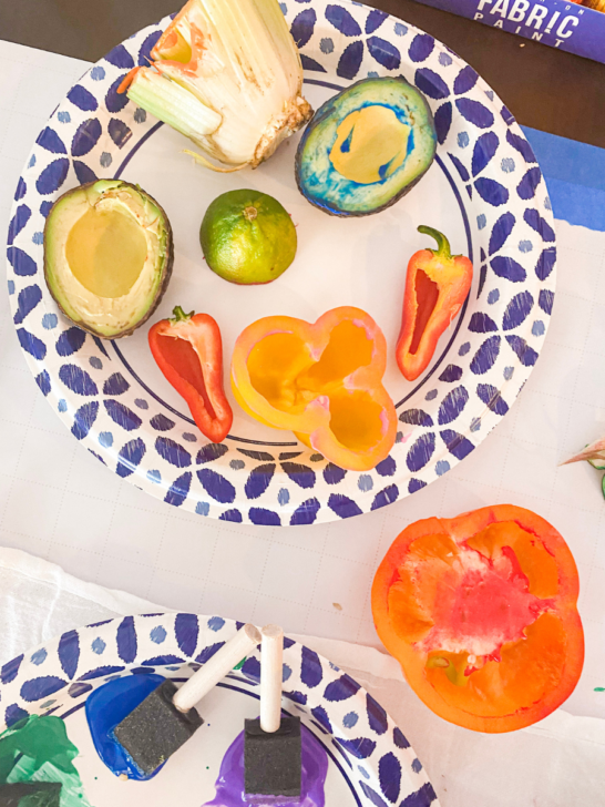 Painted fruit sitting on a plate. Avocados, celery, limes, and peppers