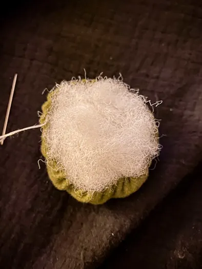 green felt with stuffing coming out the top. A thread connected on the left hand side that leads to a needle