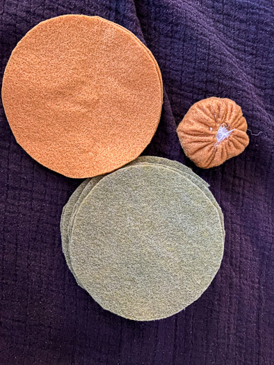 orange felt circles on the top left, green felt circles on the bottom, next to an orange felt ball with stuffing on the right.