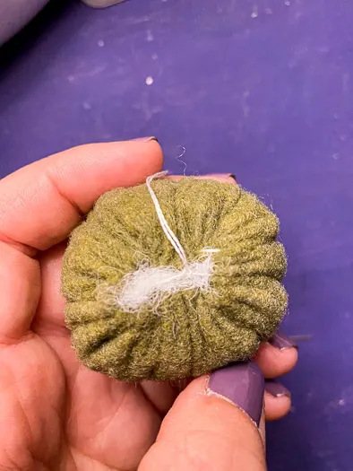 a hand holding the top of a green felt pumpkin with stuffing and embroidery thread coming out the top