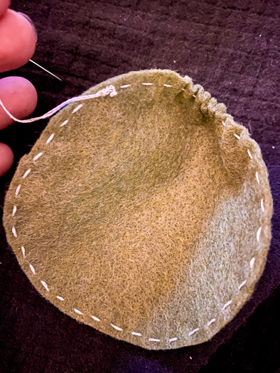 A green felt circle with white stitching around it and the felt is starting to bunch up on the right hand side.