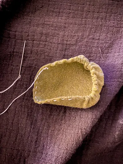 green felt with stitching and the felt is stating to bunch up to create a circle. Thread is coming off the left hand side attached to a needle