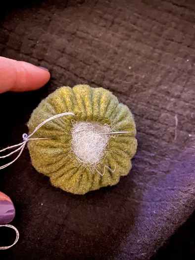 green felt ball with stuffing coming out the top and a needle inserted on the left side