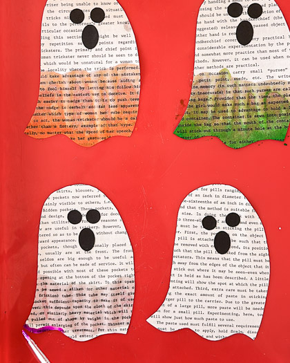 4 book page ghosts on a red tray, top 2 painted, left orange, right green, showing bottom left ghost with water on the bottom half of the ghost and starting to paint purple on the very bottom left corner