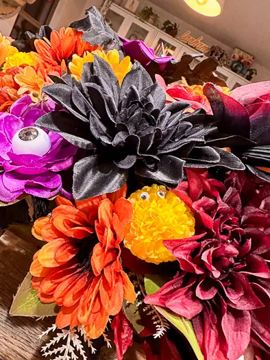 Red, orange, and purple flowers in a black basket sitting on a kitchen island. The flowers have little monster mouths, eyes, and skeleton hands.