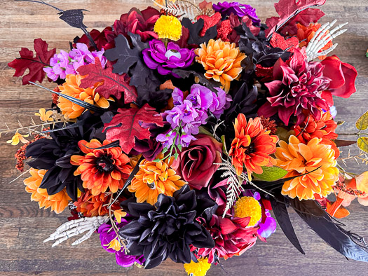 Red, orange, and purple flowers in a black basket sitting on a kitchen island. The flowers have little monster mouths, eyes, and skeleton hands.