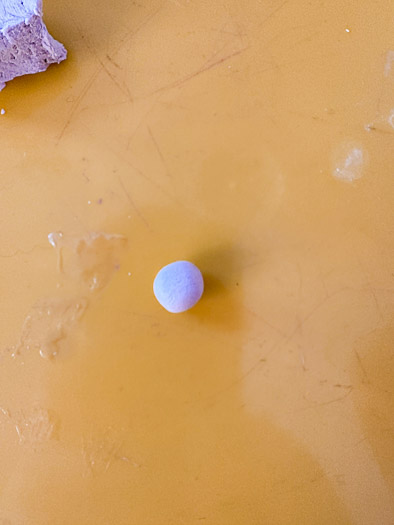 A small ball of clay sitting on a yellow board.