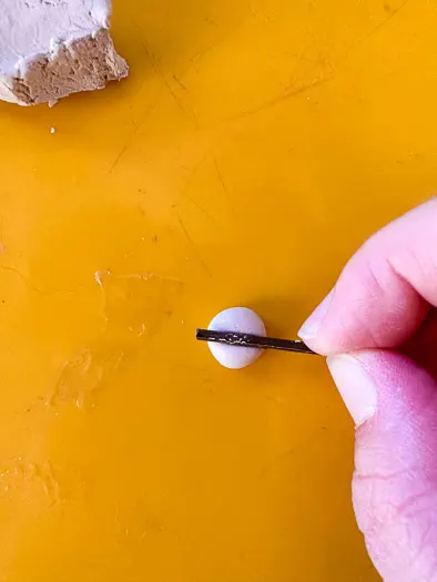 A person holding a small piece of metal squishing a small ball of clay in half.