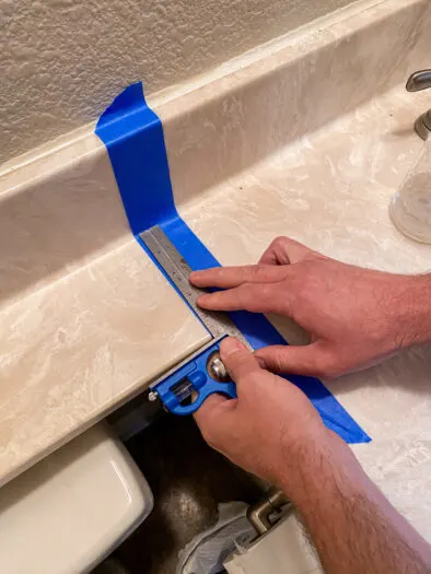 blue tape stuck onto a counter top with hands holding a straight edge on top of it